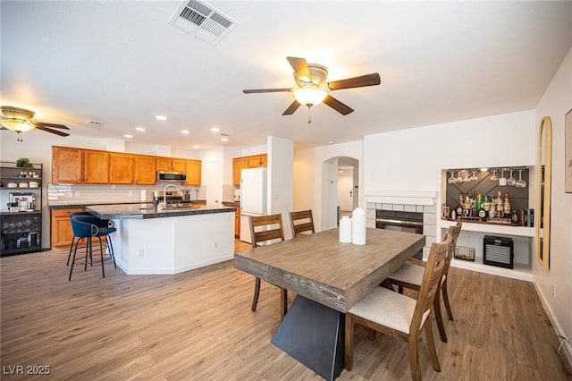 dining area with arched walkways, visible vents, light wood-style flooring, and a tile fireplace