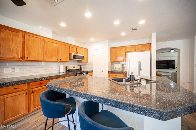 kitchen featuring stainless steel appliances, a sink, a kitchen breakfast bar, brown cabinets, and a center island with sink