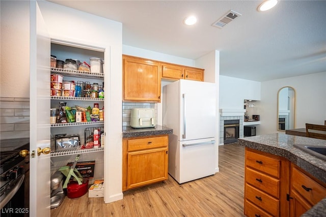 interior space with tasteful backsplash, visible vents, light wood-style floors, freestanding refrigerator, and a tile fireplace