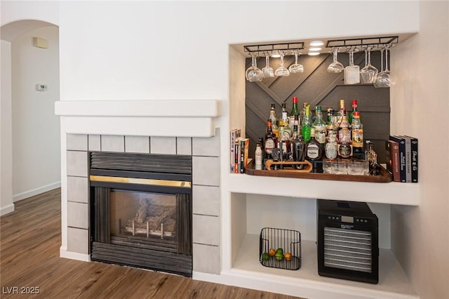 bar with a tiled fireplace, wood finished floors, and baseboards