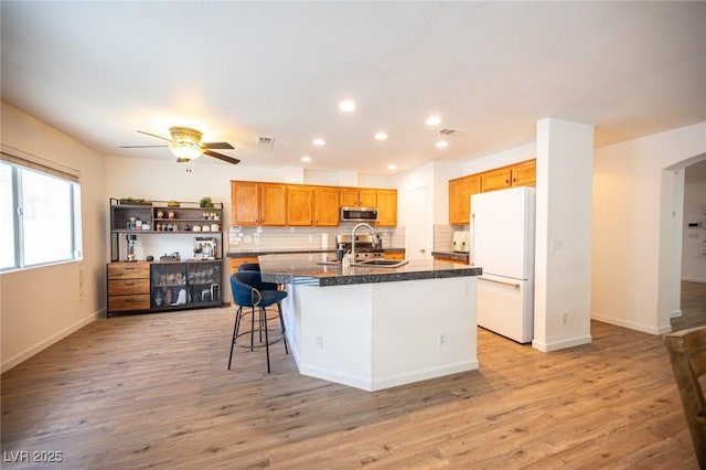 kitchen with freestanding refrigerator, stainless steel microwave, a center island with sink, and a kitchen bar