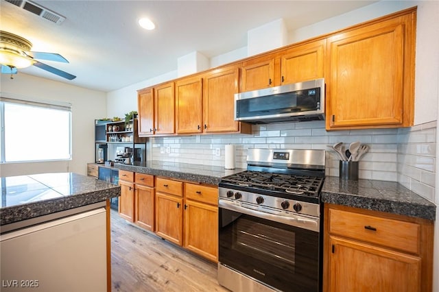 kitchen featuring tile countertops, stainless steel appliances, tasteful backsplash, visible vents, and light wood-type flooring