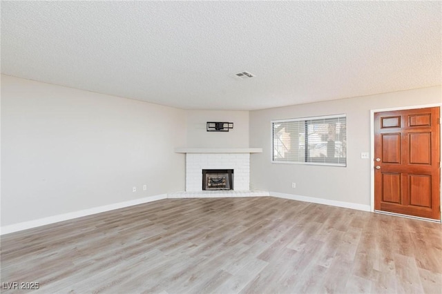 unfurnished living room featuring light wood finished floors, visible vents, baseboards, a textured ceiling, and a brick fireplace