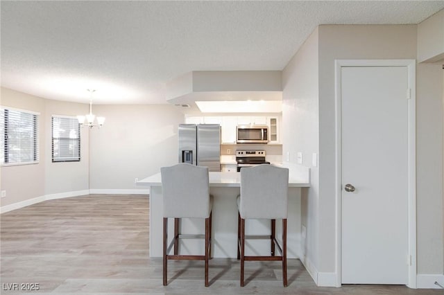 kitchen featuring stainless steel appliances, light countertops, hanging light fixtures, white cabinetry, and a kitchen bar