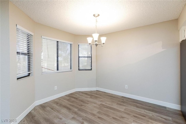 spare room with an inviting chandelier, a textured ceiling, baseboards, and wood finished floors