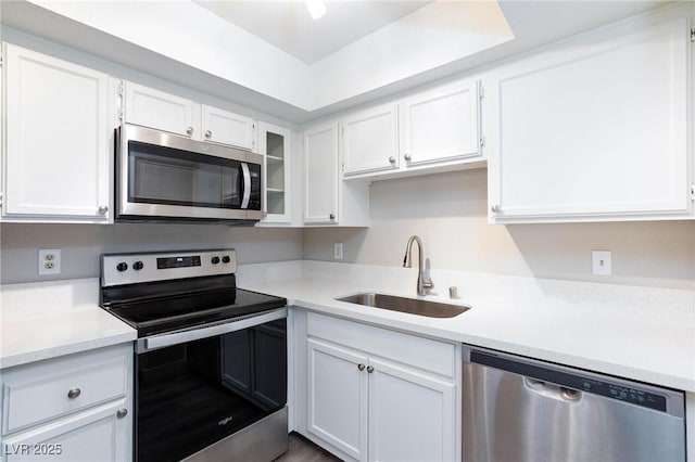 kitchen with light countertops, appliances with stainless steel finishes, glass insert cabinets, white cabinetry, and a sink