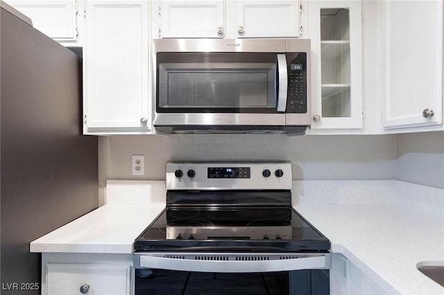 kitchen with appliances with stainless steel finishes, light countertops, white cabinetry, and glass insert cabinets