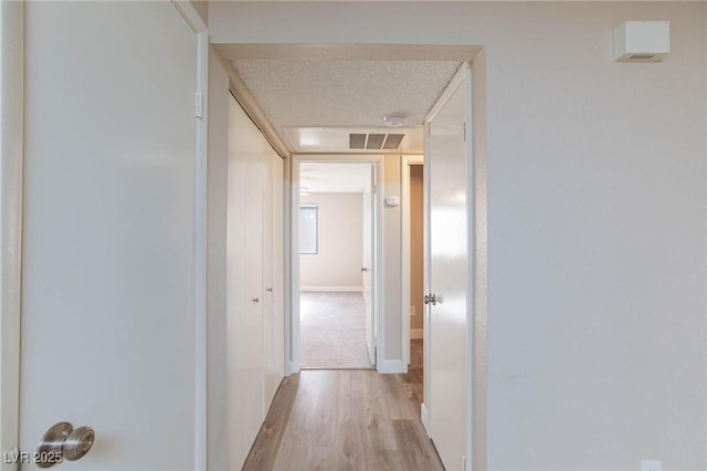 hallway featuring light wood-type flooring, visible vents, a textured ceiling, and baseboards