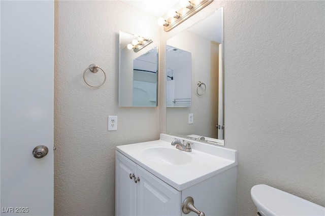 bathroom featuring toilet, a textured wall, and vanity