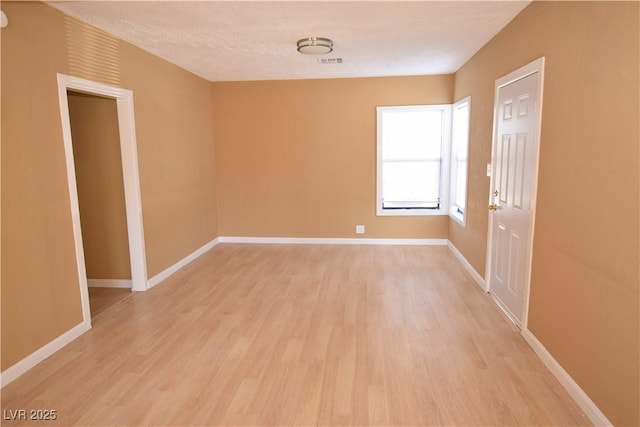 unfurnished room featuring a textured ceiling, light wood-type flooring, visible vents, and baseboards