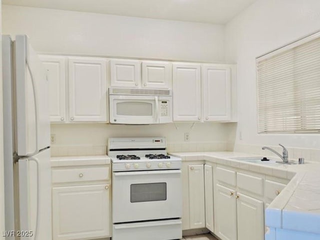 kitchen with tile countertops, white appliances, a sink, and white cabinetry