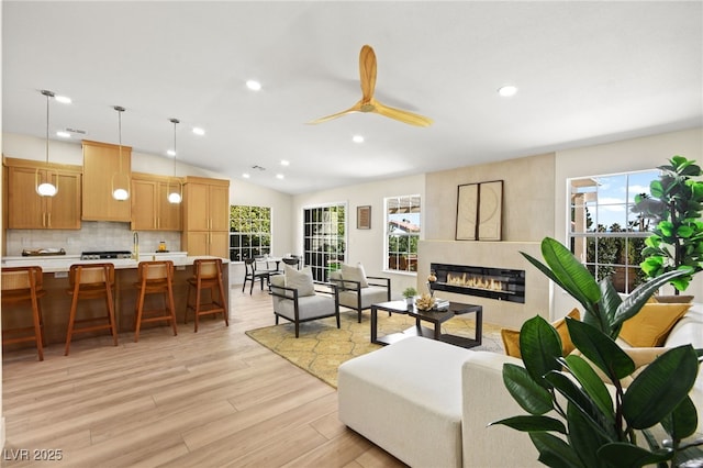 living area with light wood finished floors, recessed lighting, a tiled fireplace, vaulted ceiling, and ceiling fan