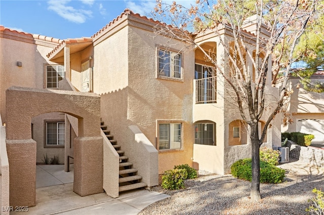 view of front facade featuring a tile roof, stairs, a patio, and stucco siding