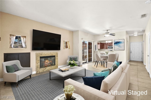 living room featuring light tile patterned floors, visible vents, a ceiling fan, a glass covered fireplace, and baseboards