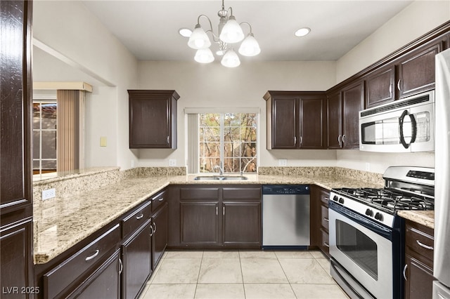 kitchen featuring light stone counters, a peninsula, hanging light fixtures, stainless steel appliances, and a sink