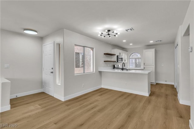 kitchen with a peninsula, visible vents, white cabinets, light countertops, and stainless steel microwave