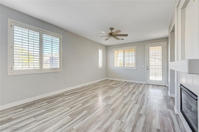 unfurnished living room with baseboards, a tile fireplace, a ceiling fan, and light wood-style floors