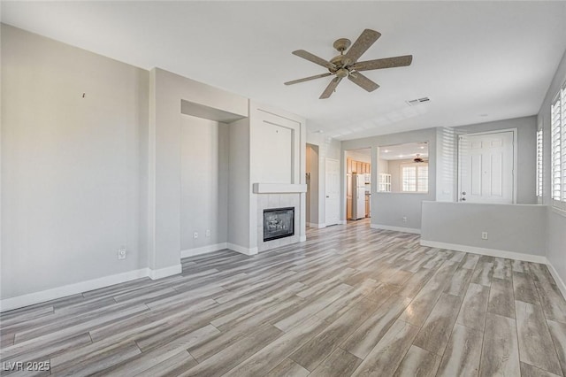 unfurnished living room with light wood-style flooring, a fireplace, visible vents, and a ceiling fan