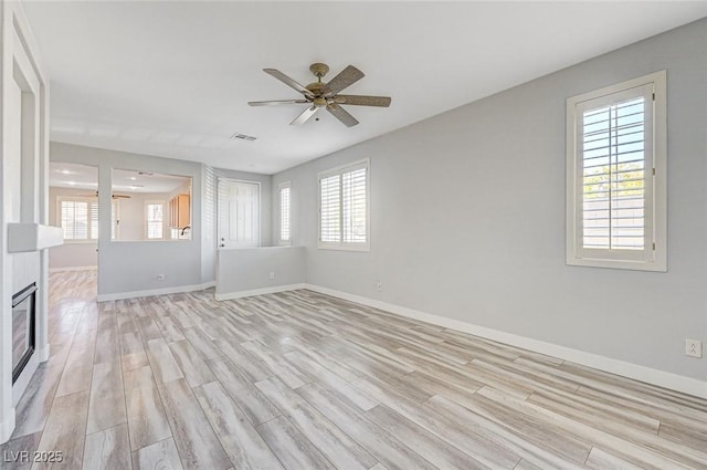 unfurnished living room featuring a glass covered fireplace, ceiling fan, light wood-style flooring, and baseboards