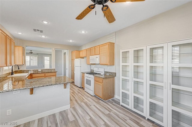 kitchen featuring a breakfast bar area, a peninsula, white appliances, a sink, and visible vents