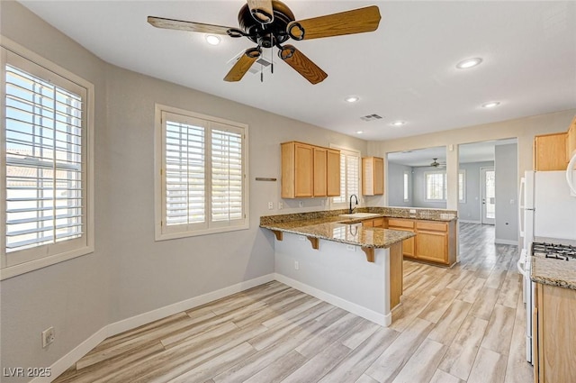 kitchen with visible vents, light wood-style floors, a sink, a peninsula, and a kitchen breakfast bar