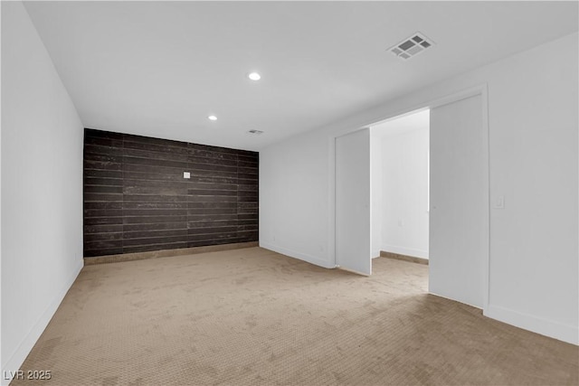 carpeted empty room featuring an accent wall, wooden walls, visible vents, and recessed lighting