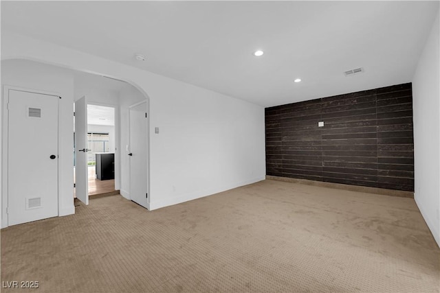 spare room featuring light carpet, wood walls, visible vents, and arched walkways