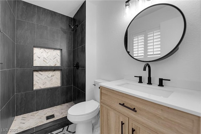 full bathroom featuring toilet, a tile shower, and vanity