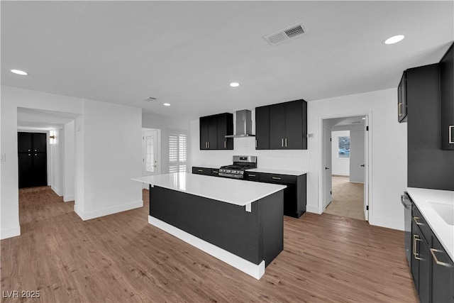 kitchen featuring stainless steel gas stove, visible vents, wall chimney exhaust hood, dark cabinets, and light countertops