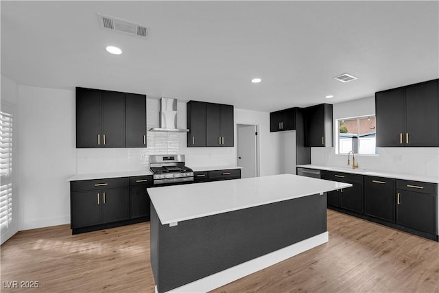 kitchen featuring dark cabinets, visible vents, wall chimney exhaust hood, and gas range