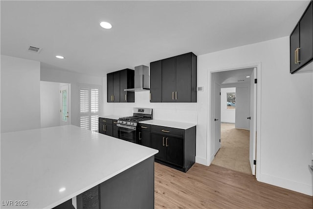 kitchen with light countertops, stainless steel range with gas cooktop, dark cabinetry, and wall chimney range hood