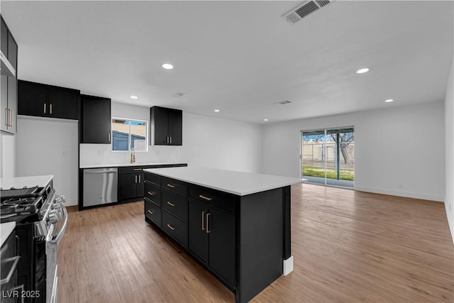 kitchen with light wood-style flooring, a kitchen island, dark cabinets, stainless steel appliances, and light countertops