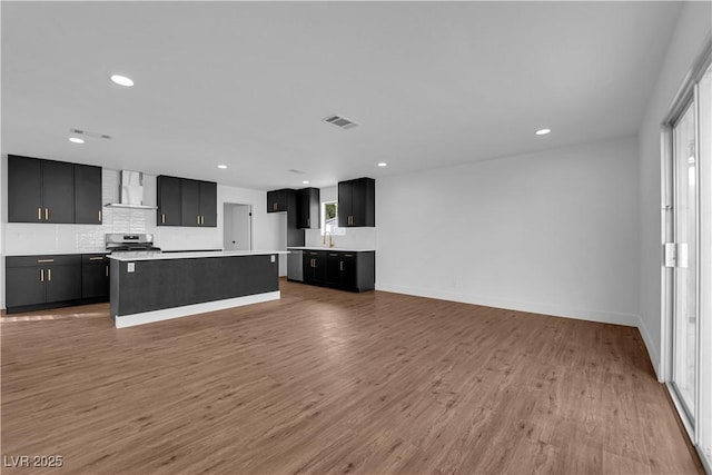 kitchen with dark cabinetry, light wood-type flooring, wall chimney range hood, and visible vents