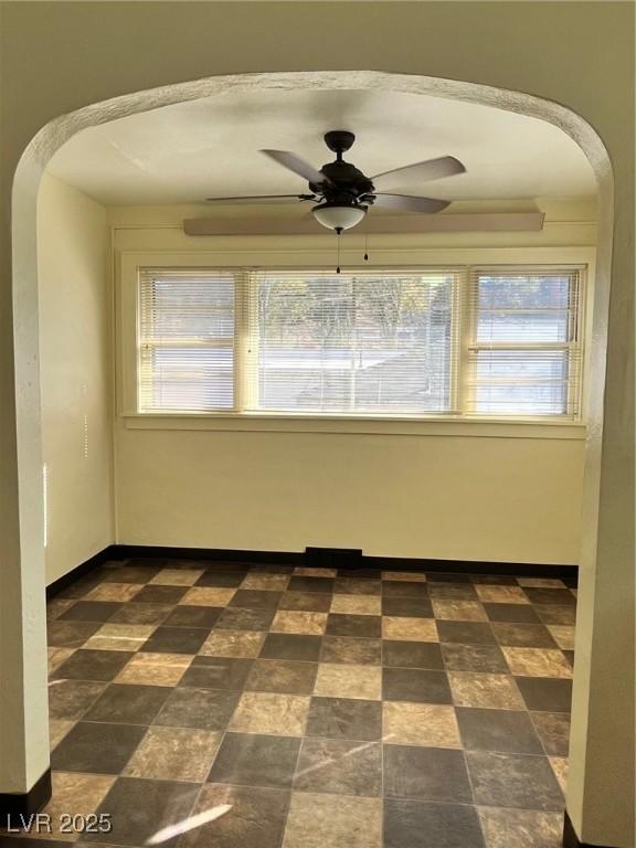 spare room featuring stone finish flooring, arched walkways, and a ceiling fan