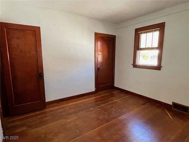 spare room featuring dark wood-style flooring, visible vents, and baseboards