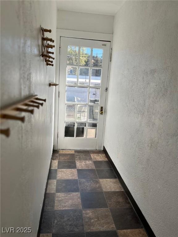 doorway to outside with a textured wall, stone tile flooring, and baseboards