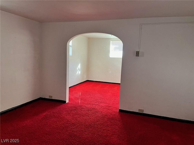 empty room with arched walkways, carpet flooring, and baseboards