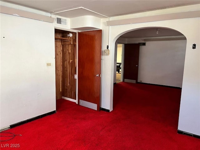 empty room featuring arched walkways, visible vents, dark carpet, and baseboards