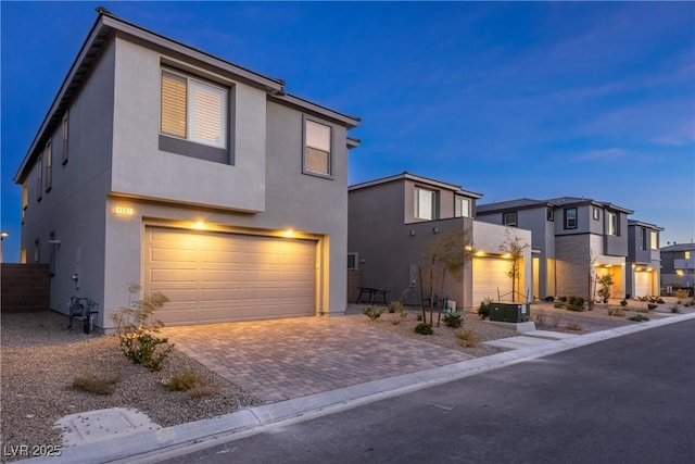 modern home featuring decorative driveway, an attached garage, a residential view, and stucco siding