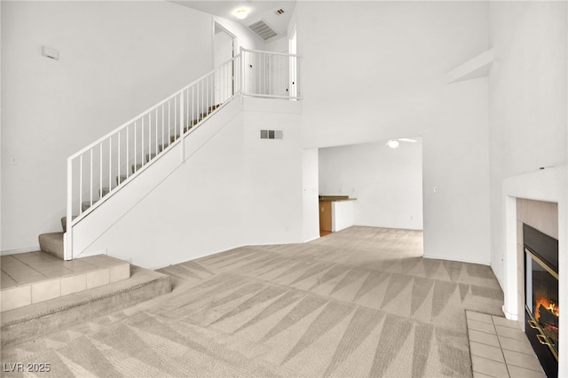 unfurnished living room with light carpet, a fireplace, a towering ceiling, visible vents, and stairs