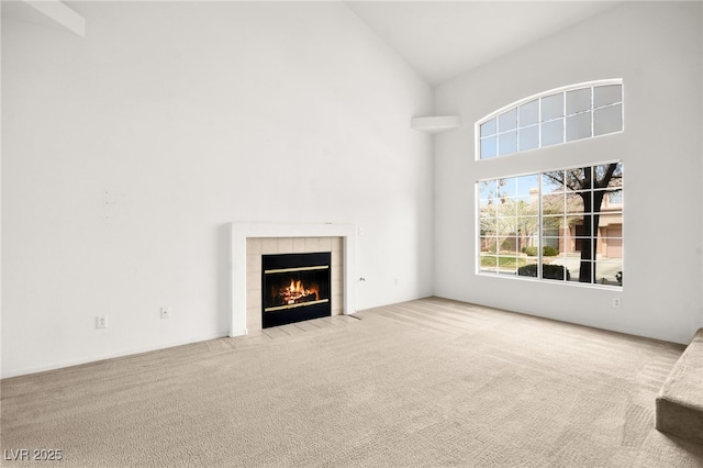 unfurnished living room with light carpet, high vaulted ceiling, and a tile fireplace