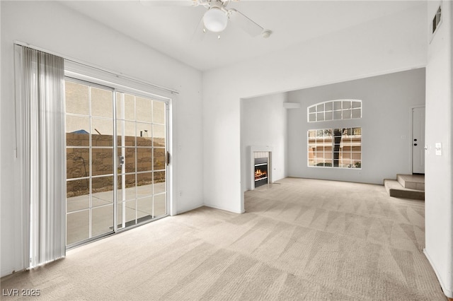 unfurnished living room with light carpet, a fireplace with flush hearth, visible vents, and a ceiling fan