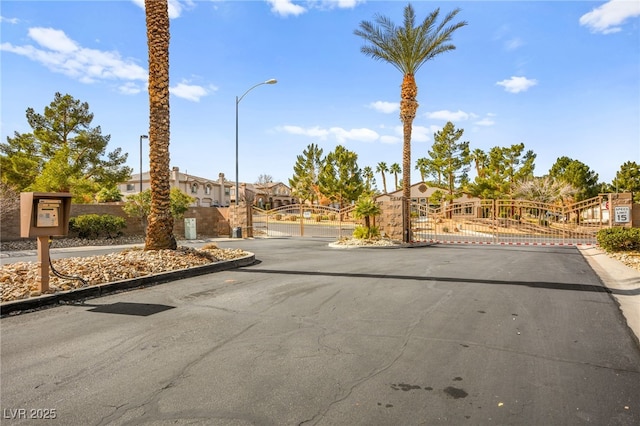 view of street featuring a gate, a gated entry, street lights, and curbs