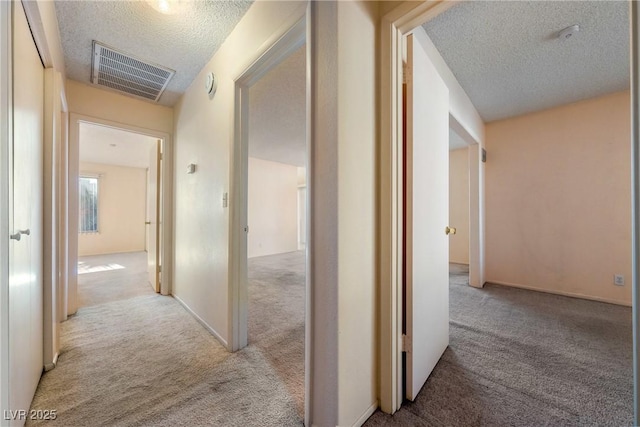 hallway featuring a textured ceiling, visible vents, and light colored carpet