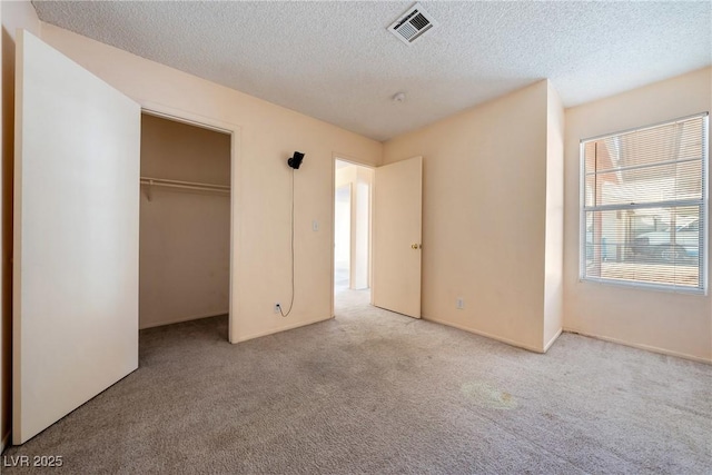 unfurnished bedroom featuring a closet, visible vents, light carpet, and a textured ceiling