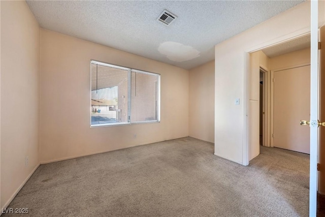 unfurnished room featuring light colored carpet, visible vents, and a textured ceiling