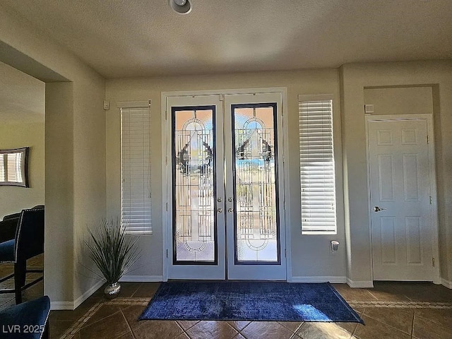 interior space with a wealth of natural light, french doors, dark tile patterned floors, and baseboards