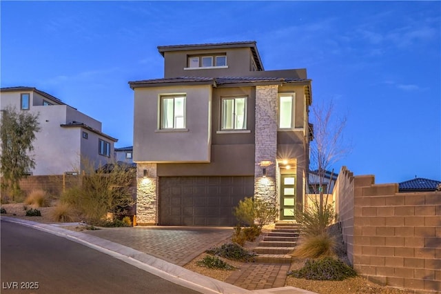 view of front facade featuring decorative driveway, stucco siding, fence, a garage, and stone siding