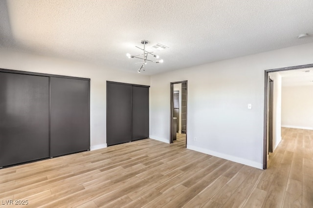 unfurnished bedroom with a chandelier, visible vents, light wood finished floors, and two closets