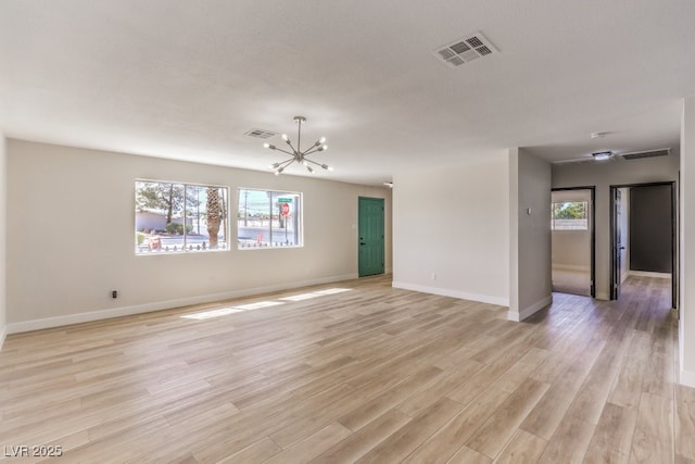 empty room featuring an inviting chandelier, light wood-style flooring, visible vents, and baseboards